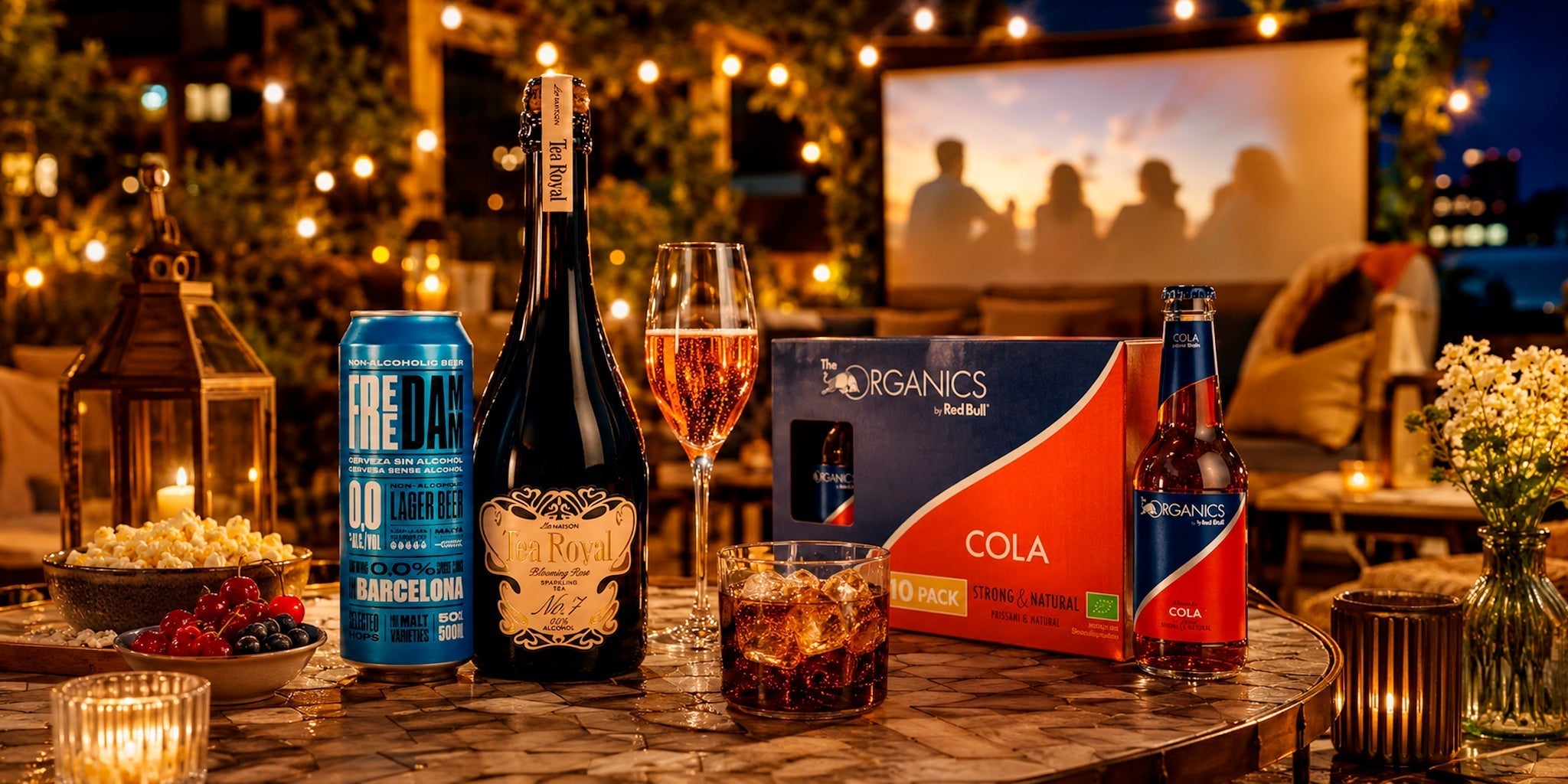 Alcohol-free summer movie night drinks with Free Damm 0.0 beer, Tea Royal sparkling tea and Red Bull Organics Cola on a cozy outdoor cinema table.