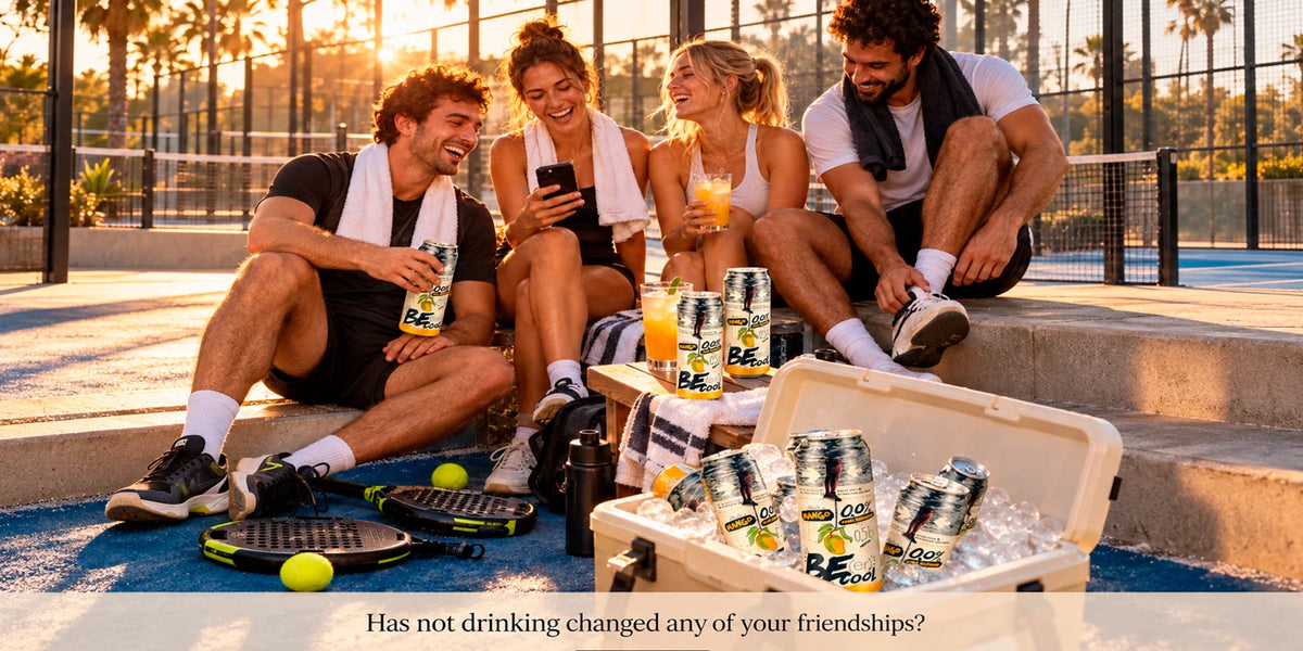 BE Cool Mango 0.0 alcohol-free drinks served chilled after a padel match, with four friends relaxing courtside at sunset beside rackets, tennis balls and an ice-filled cooler.
