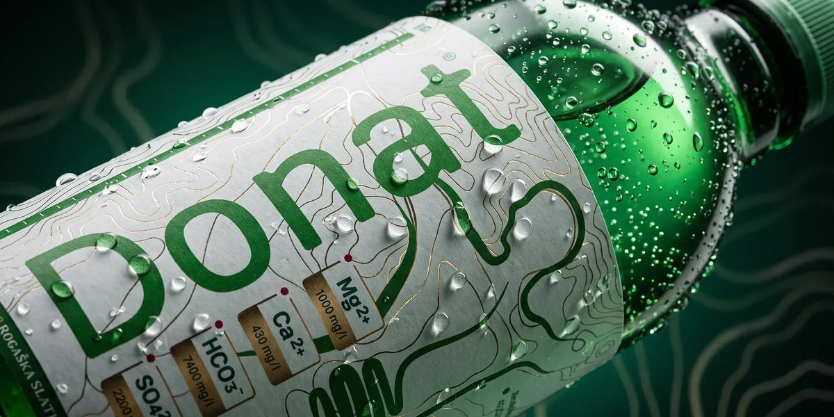Donat natural mineral water macro close-up with condensation, sparkling bubbles and visible magnesium, calcium, bicarbonate and sulfate mineral content on the label in a deep green wellness setting.