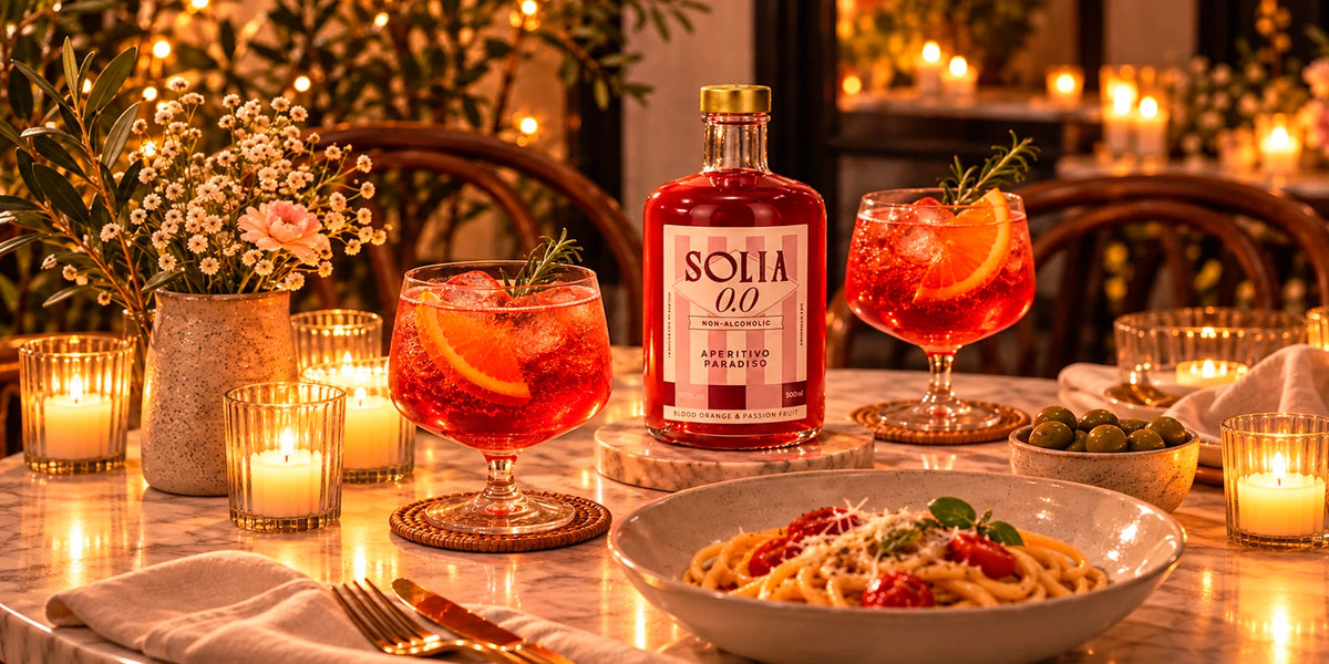 Solia 0.0 Non-Alcoholic Aperitivo Paradiso Blood Orange & Passion Fruit served in two spritz-style glasses with citrus and rosemary at a warm candlelit dinner table.